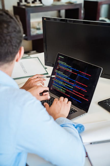 A close-up image shows a laptop computer with a visible screen displaying lines of programming code. The laptop is placed on a wooden surface, and beside it is a ceramic coffee mug with a beige backgr